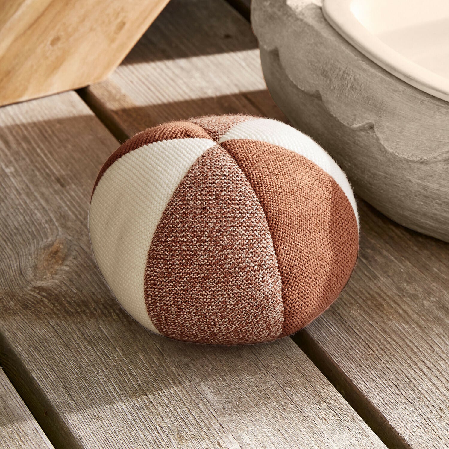 Okrągła poduszka dekoracyjna z tkaniny w brązowo-białe pasy na drewnianej podłodze