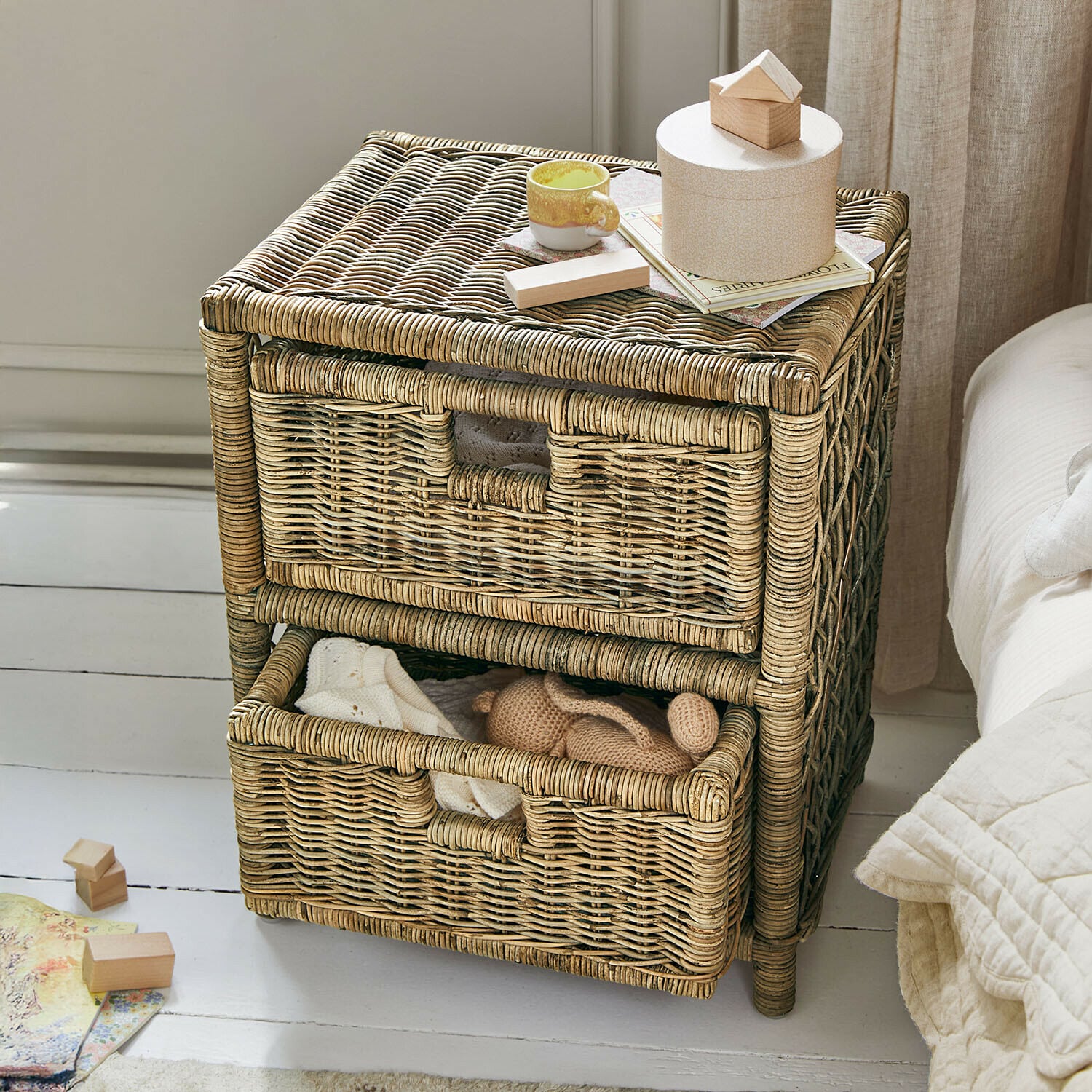 Dwukomorowa szafka z wikliny w naturalnym kolorze z dekoracjami na blacie i miękkimi tkaninami w środku