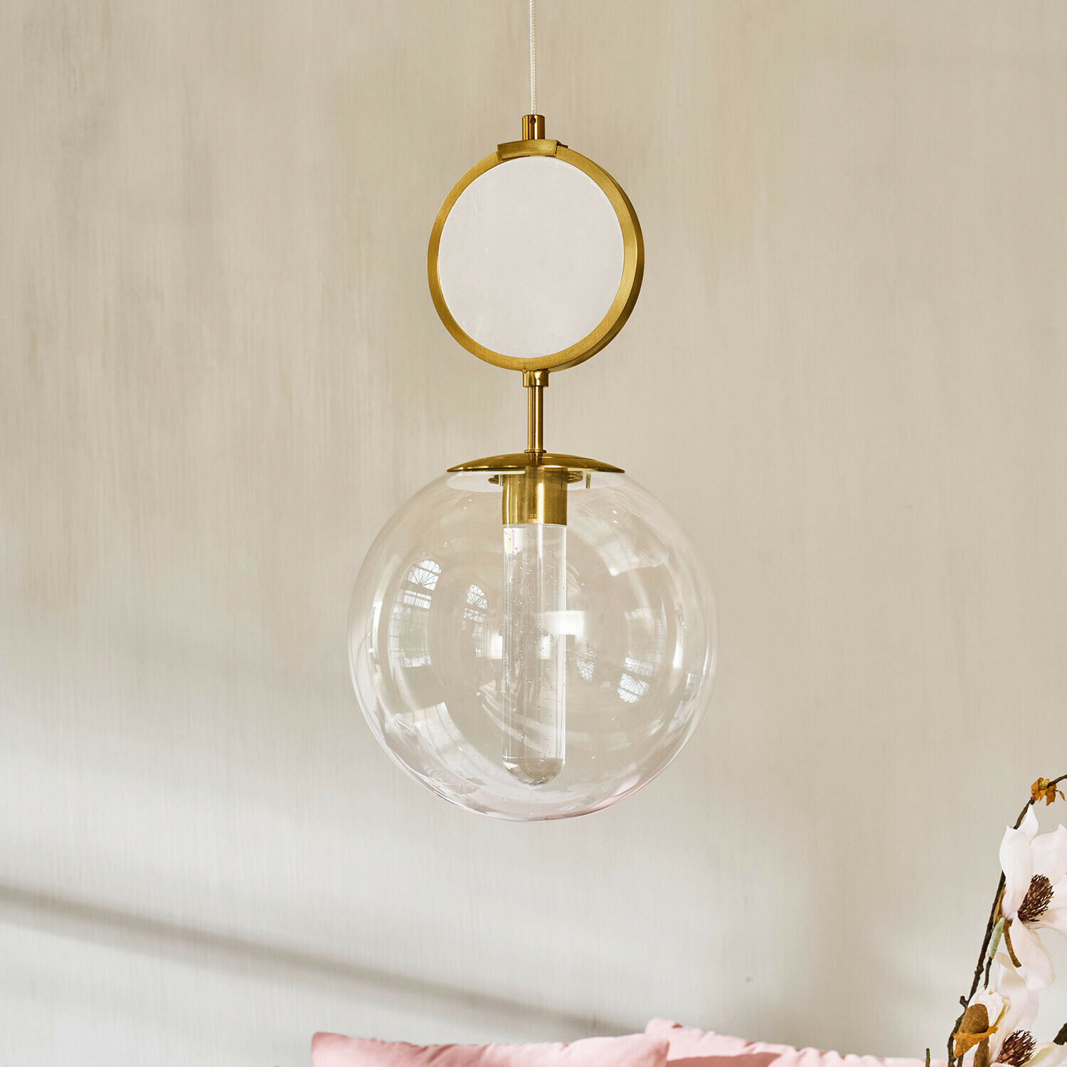 Lampa wisząca LED Corvane Złota lampa wisząca z przezroczystą szklaną kulą i dekoracyjnym okrągłym elementem na tle jasnej ściany