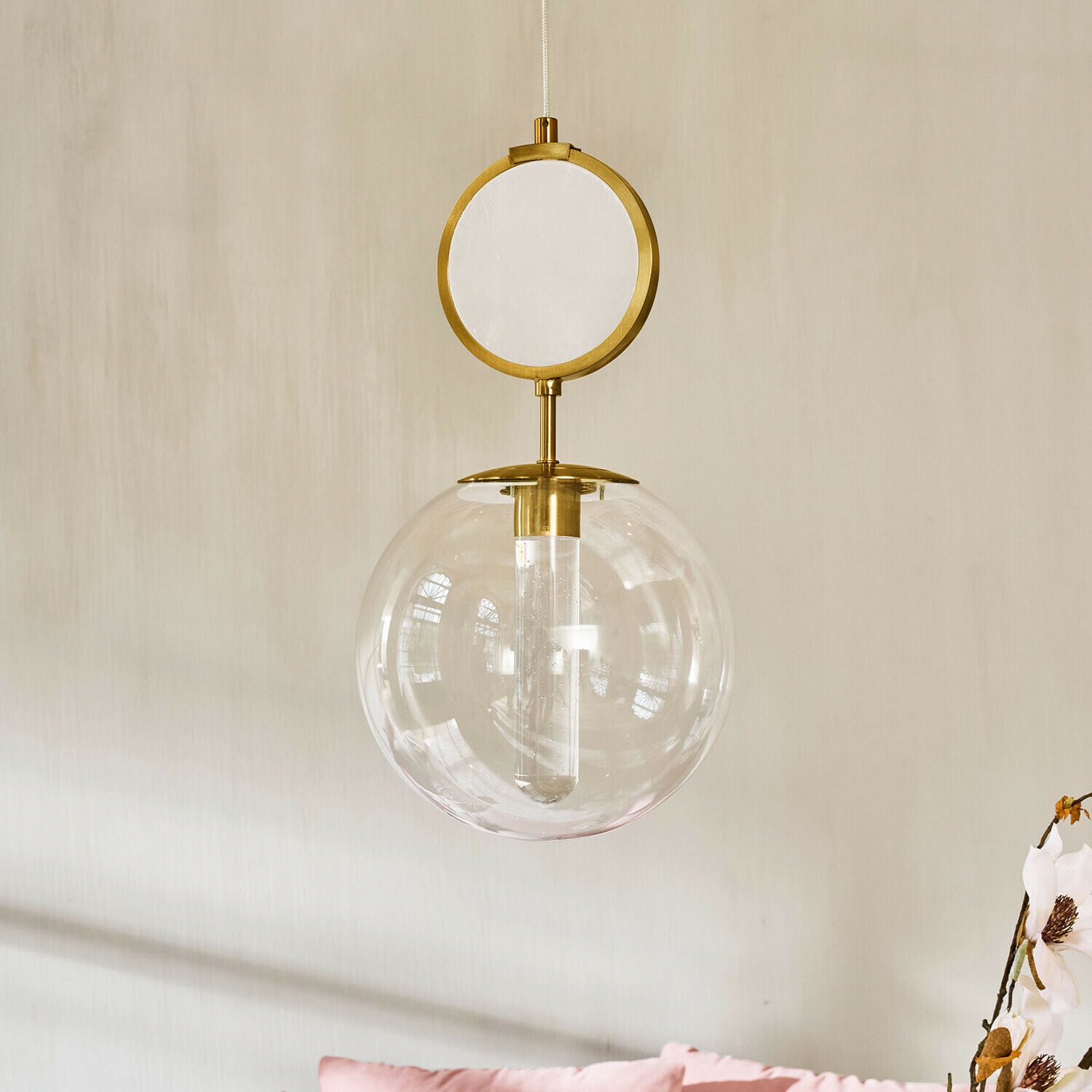Lampa wisząca LED Corvane Złota lampa wisząca z przezroczystą szklaną kulą i dekoracyjnym okrągłym elementem na tle jasnej ściany