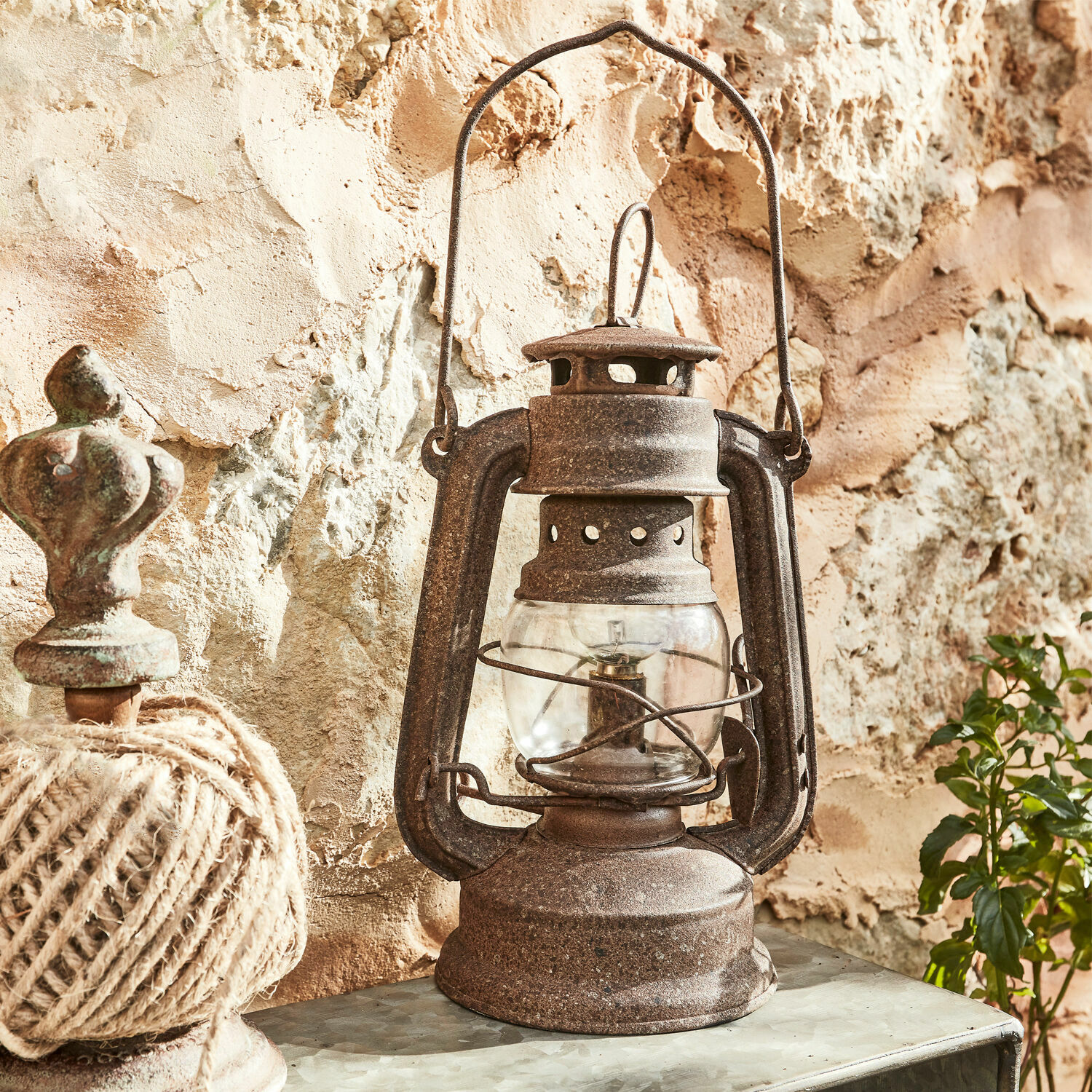 Lampion LED Oxcroft Rustykalna metalowa lampa naftowa w kolorze rdzy na tle kamiennej ściany, dekoracja vintage