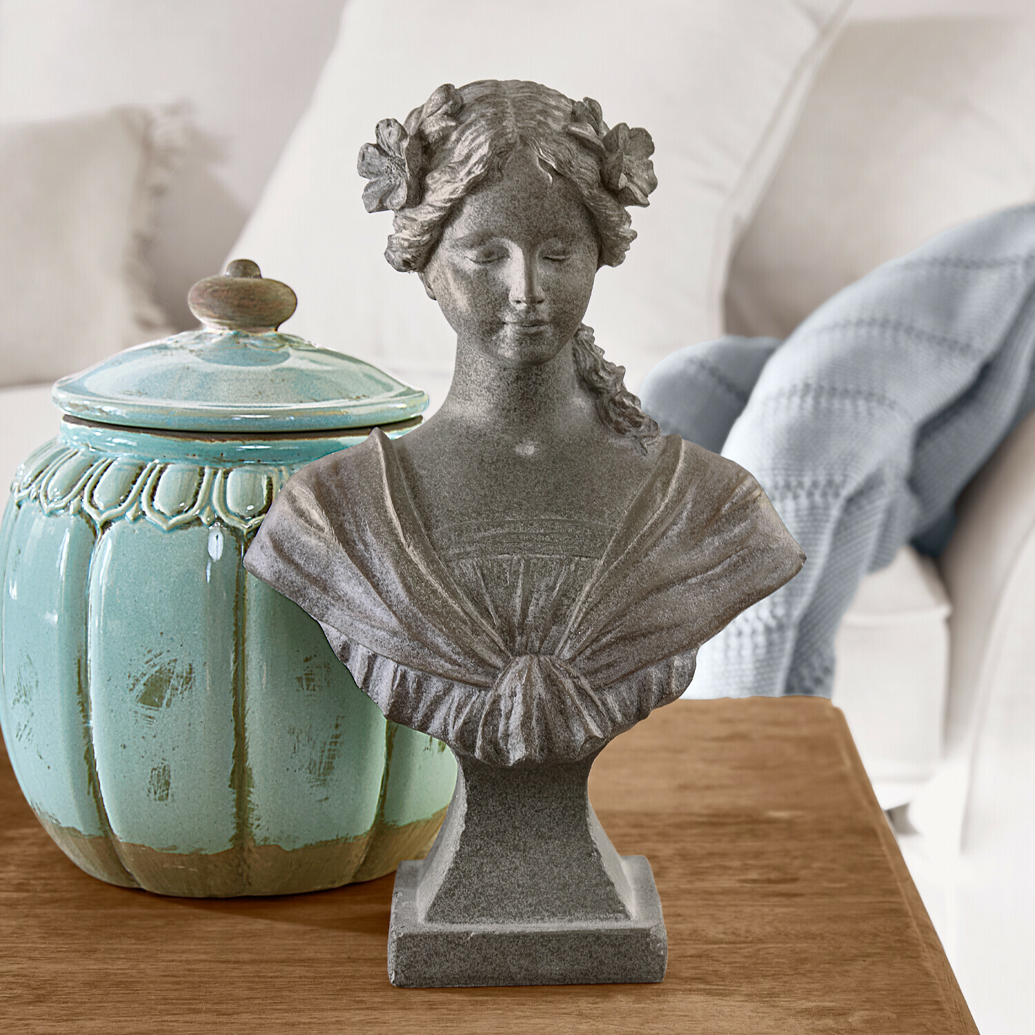 Popiersie Alexandra Popiersie kobiety z kwiatami we włosach z szarego kamienia na drewnianym stole z turkusowym ceramicznym pojemnikiem