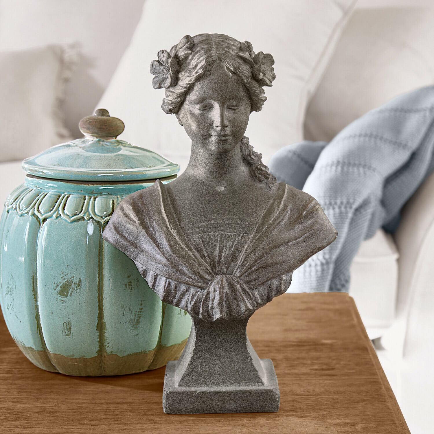 Popiersie Alexandra Popiersie kobiety z kwiatami we włosach z szarego kamienia na drewnianym stole z turkusowym ceramicznym pojemnikiem