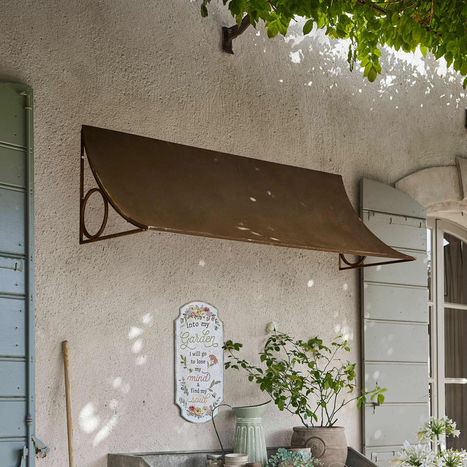 Metalowy brązowy daszek ścienny nad oknem z dekoracją ogrodową i donicą z rośliną