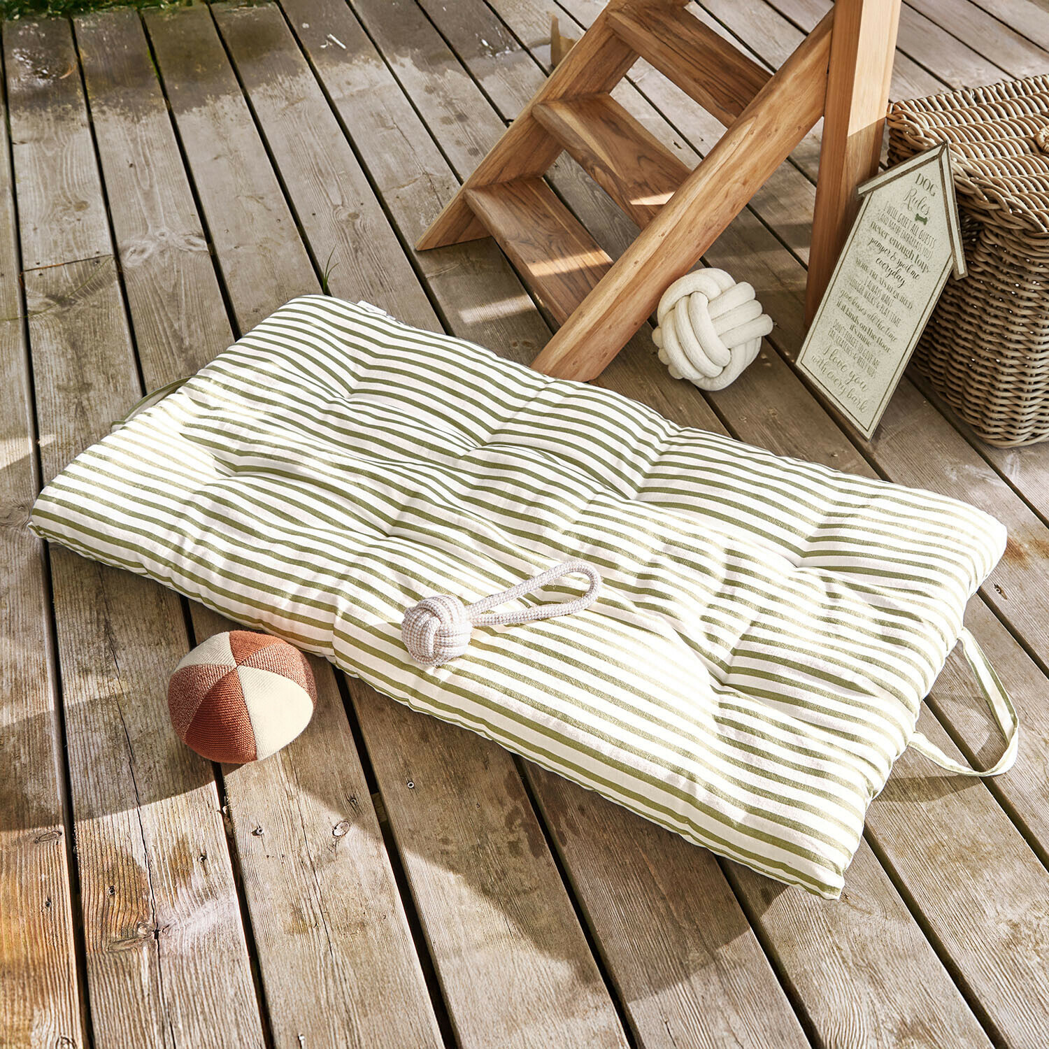 Pikowana poduszka na podłogę w zielone paski na drewnianym tarasie z zabawkami dla psa