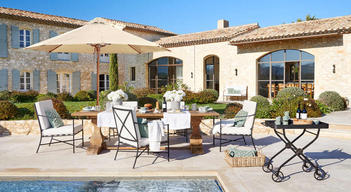 Zestaw mebli ogrodowych z drewnianym stołem i kremowymi poduszkami na tarasie przy basenie