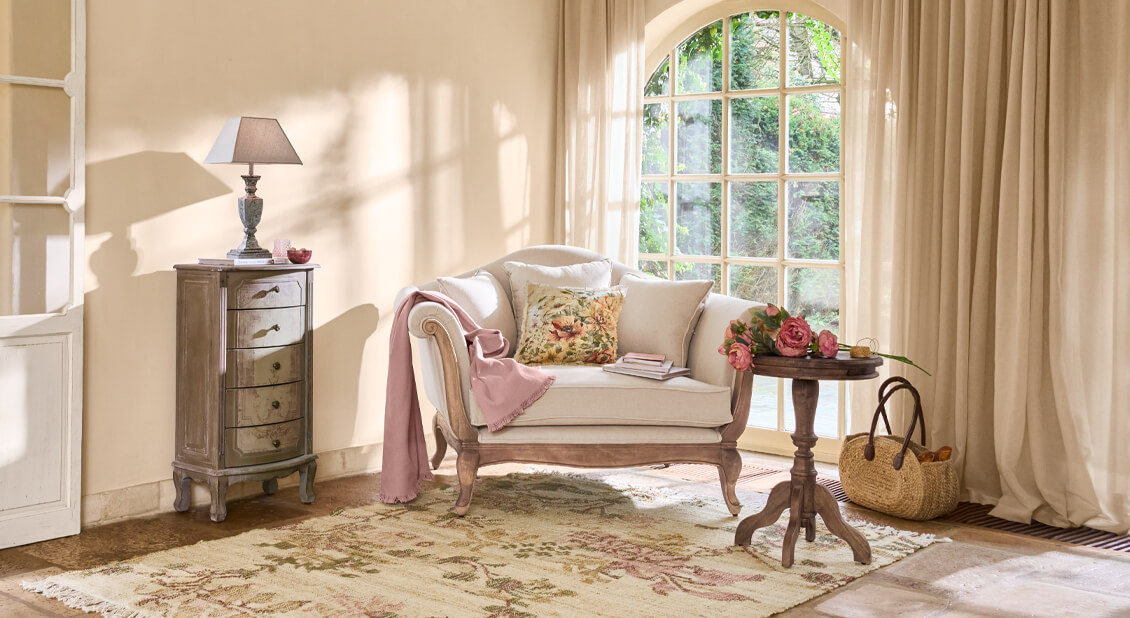 Przytulny salon z beżową sofą, różowym kocem i drewnianym stolikiem z kwiatami, naturalne światło