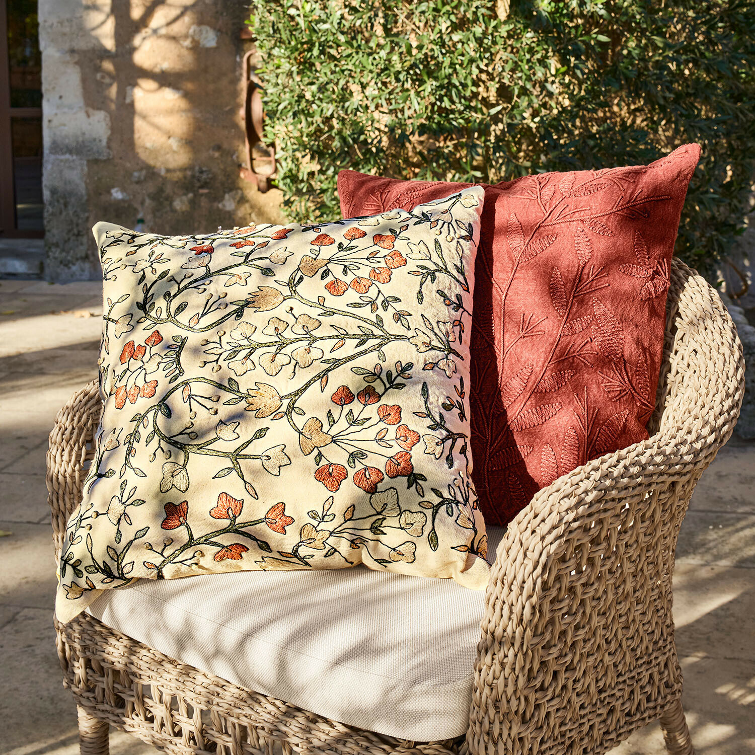 Dwa dekoracyjne poduszki z haftem kwiatowym i liściastym na wiklinowym fotelu na zewnątrz