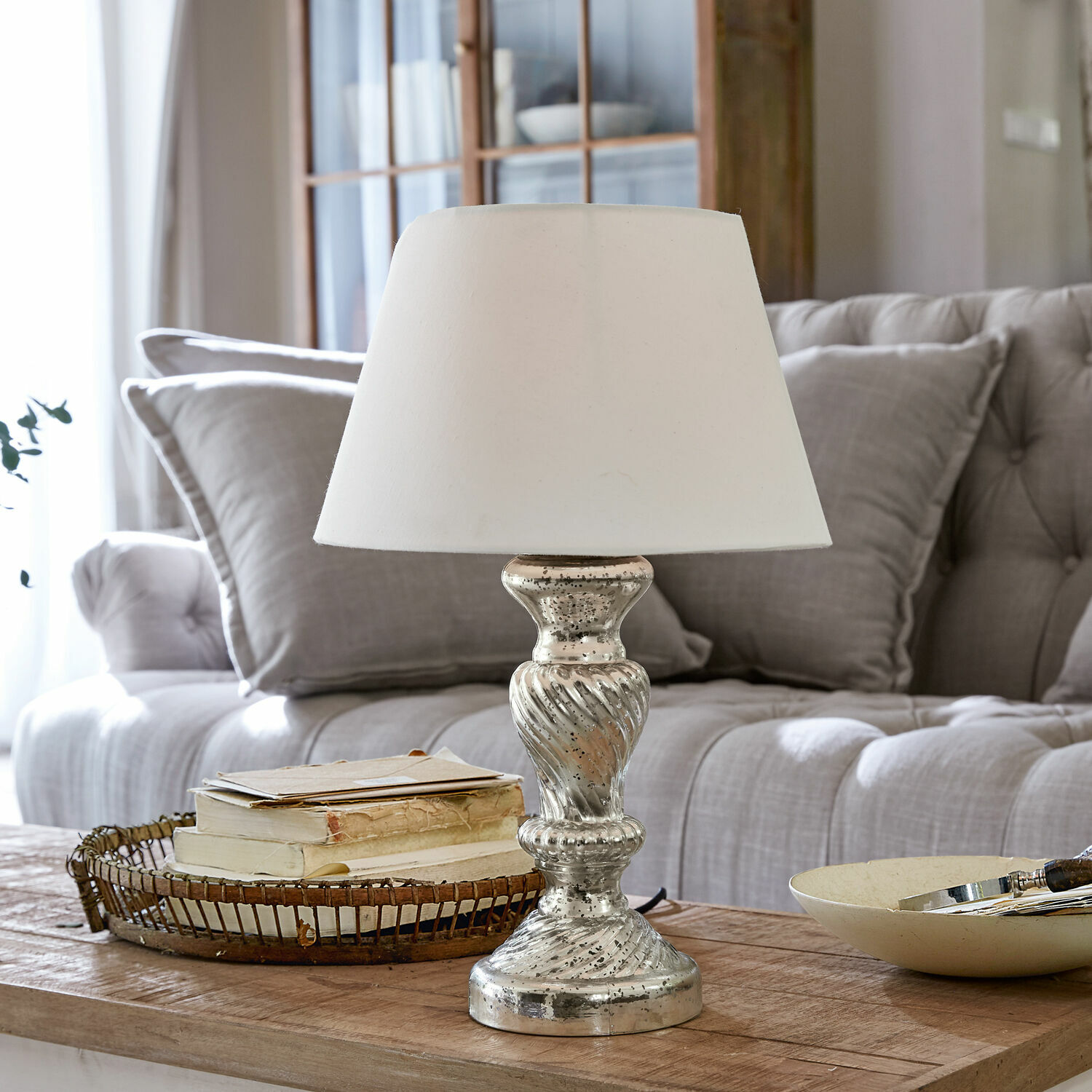 Lampa stołowa Hazel Lampka stołowa z białym abażurem i srebrną podstawą na drewnianym stole w salonie