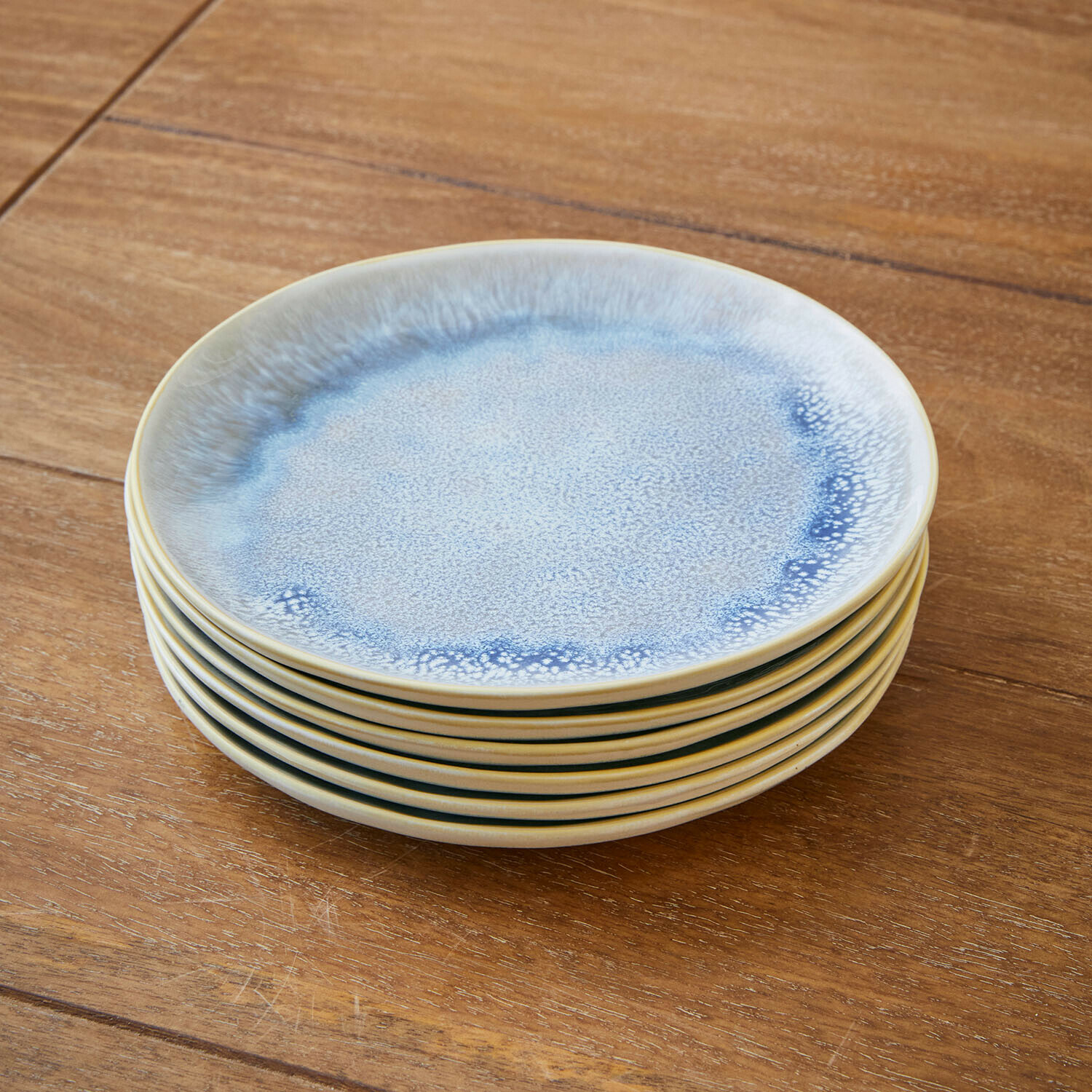 Zestaw sześciu ceramicznych talerzy w odcieniach niebieskiego i kremowego na drewnianym stole