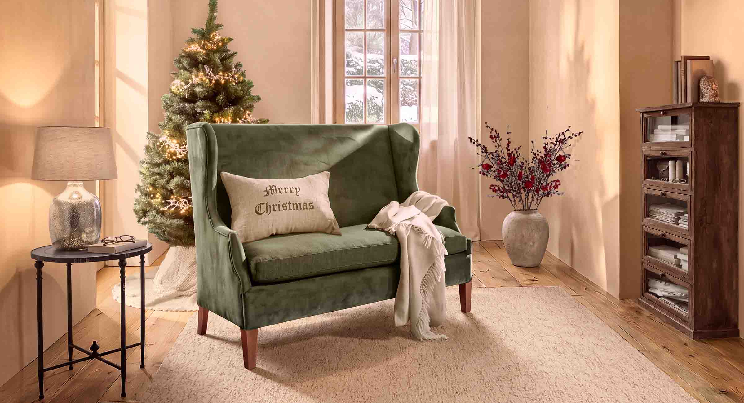 Zielona aksamitna sofa z poduszką Merry Christmas w przytulnym salonie z choinką i lampą