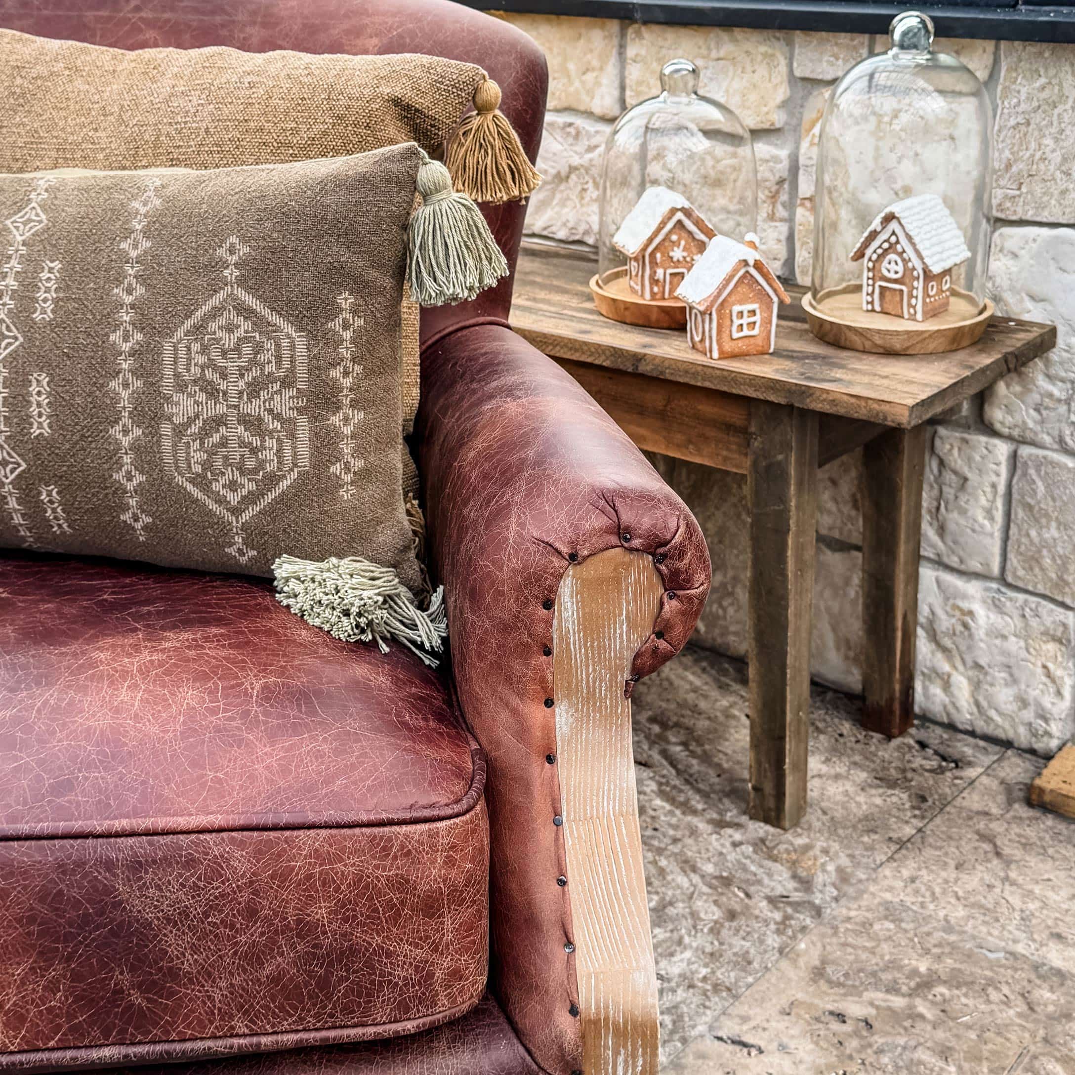 Brązowa skórzana sofa z ozdobnymi poduszkami i drewnianym stolikiem z piernikowymi domkami pod szkłem