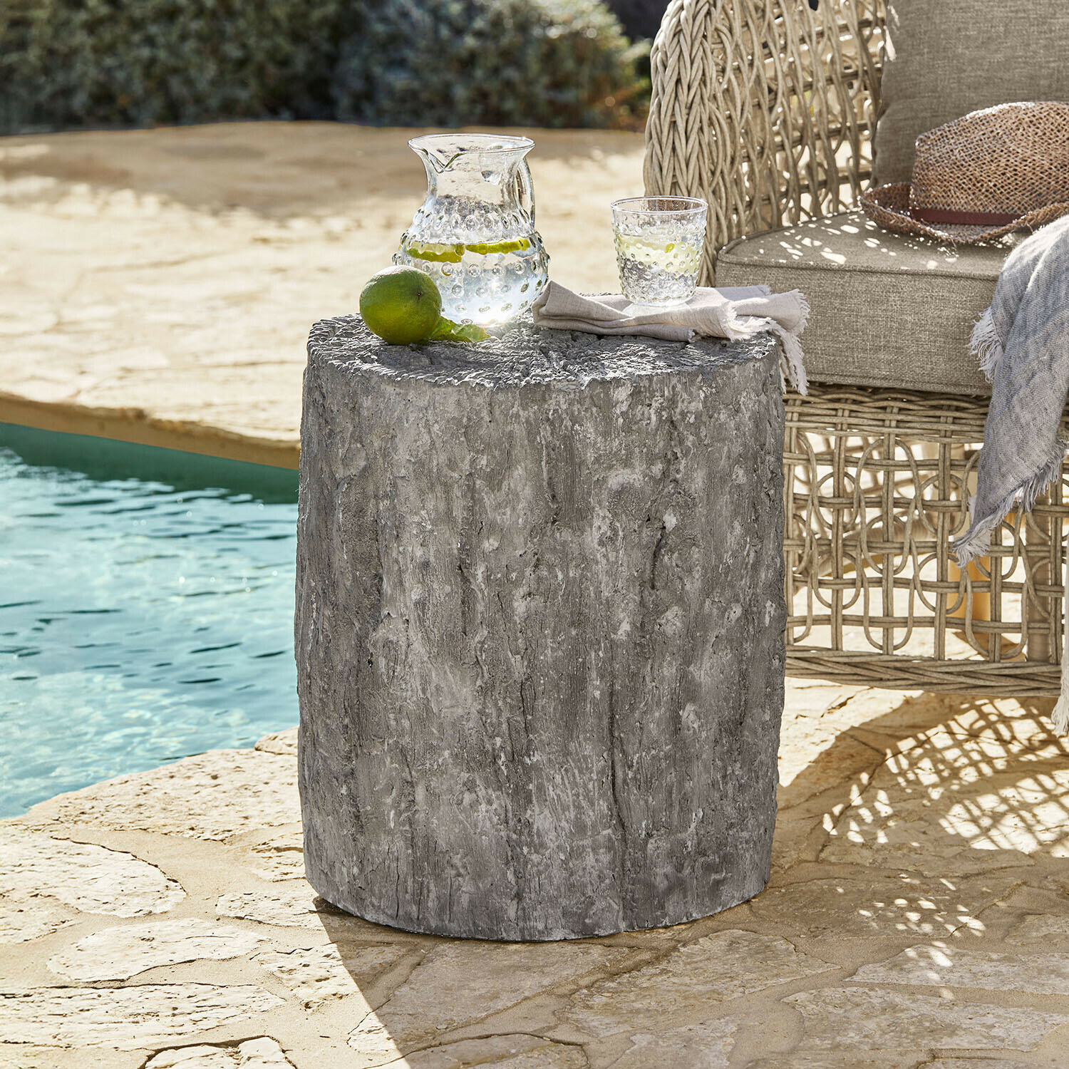 Szary stolik ogrodowy z betonu o fakturze drewna obok wiklinowego fotela przy basenie