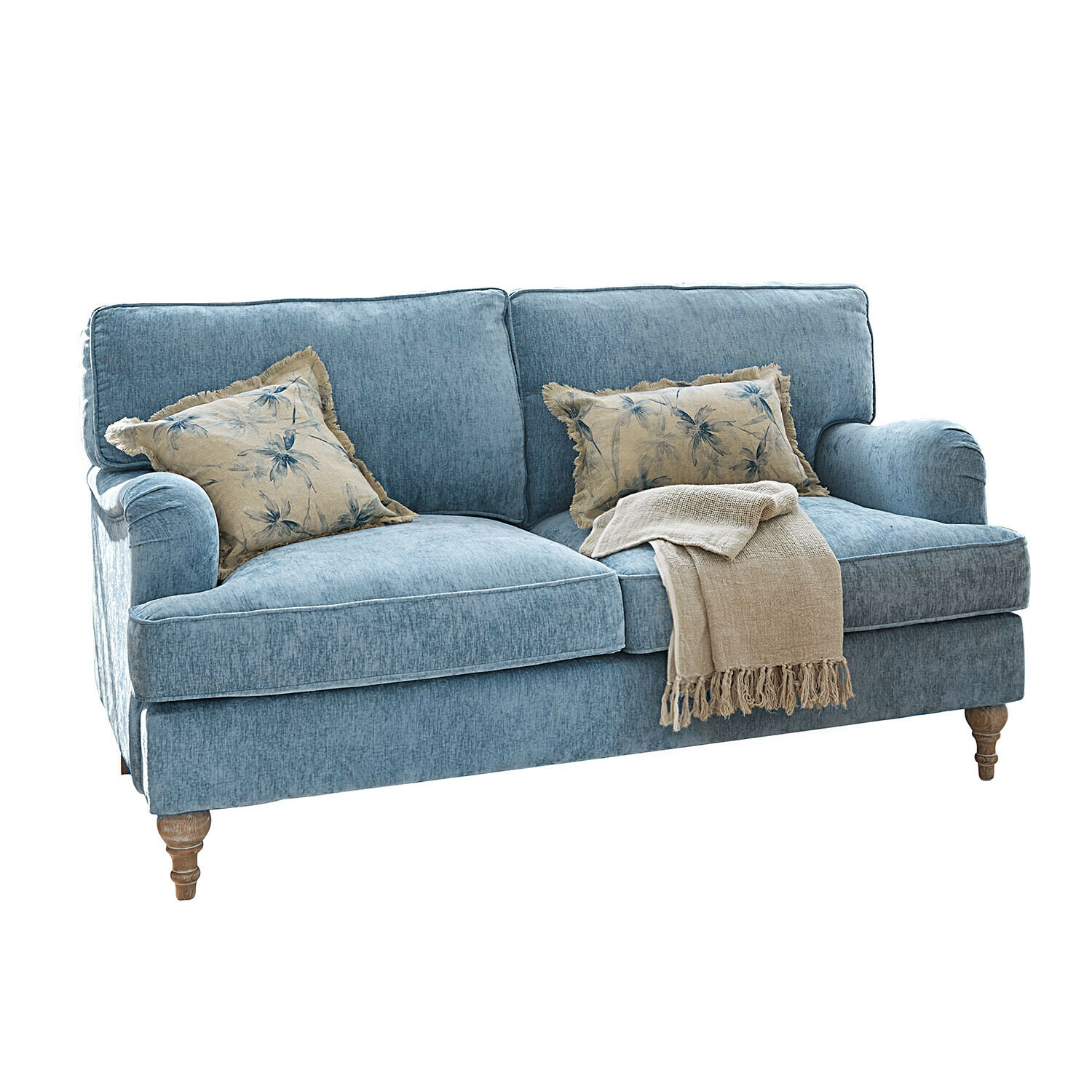 Sofa Elvika Niebieska sofa tapicerowana z drewnianymi nogami, ozdobiona beżowym kocem i poduszkami z motywem roślinnym